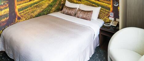 A hotel room with a large bed, a nightstand with a lamp, and a chair.