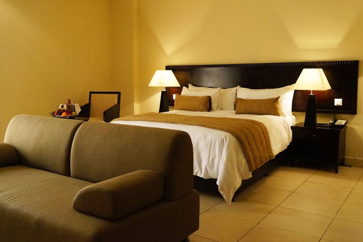 Ein Hotelzimmer mit einem Bett, zwei Nachttischen mit Lampen, einem Sofa und einer Obstschale auf dem Beistelltisch.