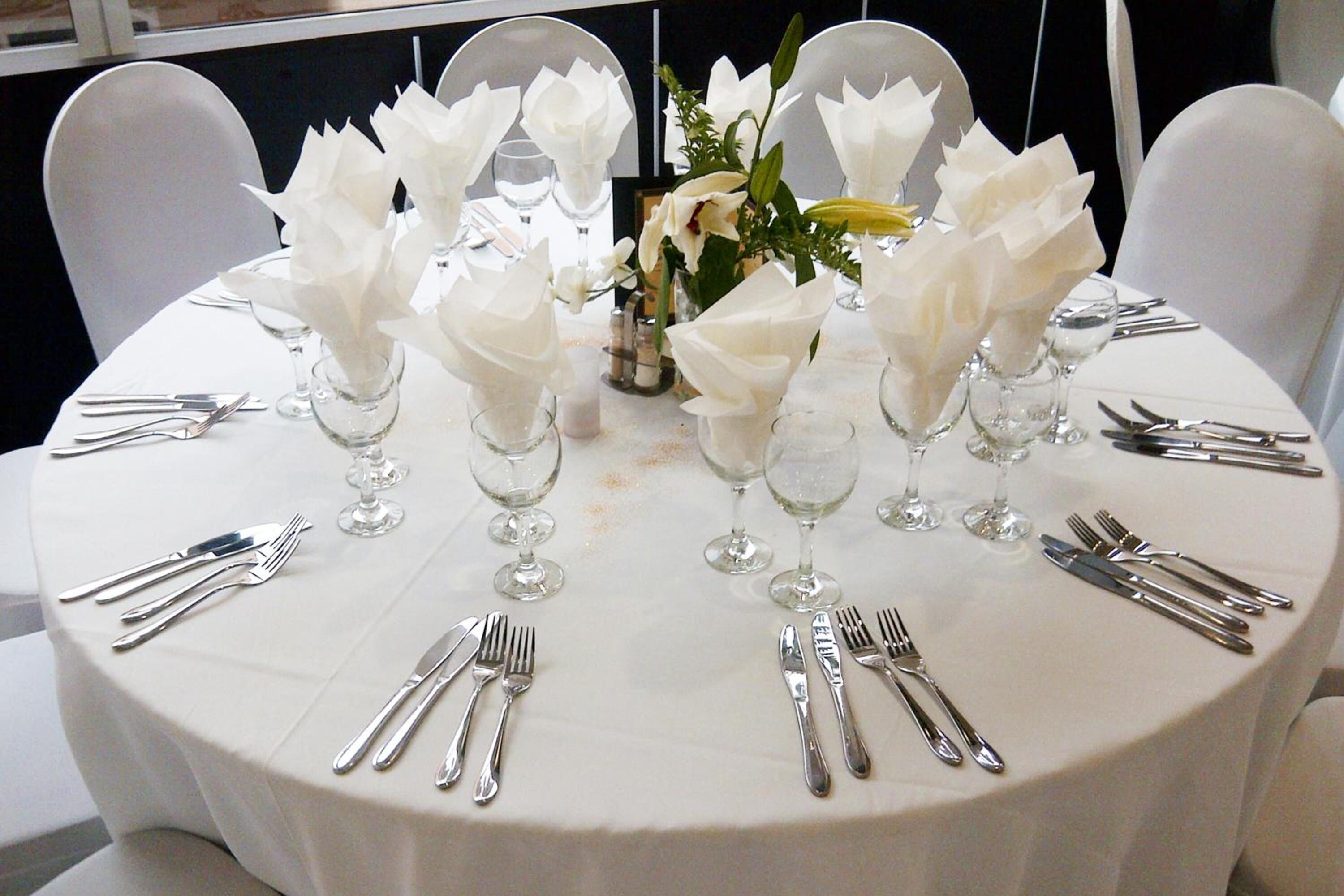 A round table set for a formal event with white tablecloth, silverware, and floral centerpieces.