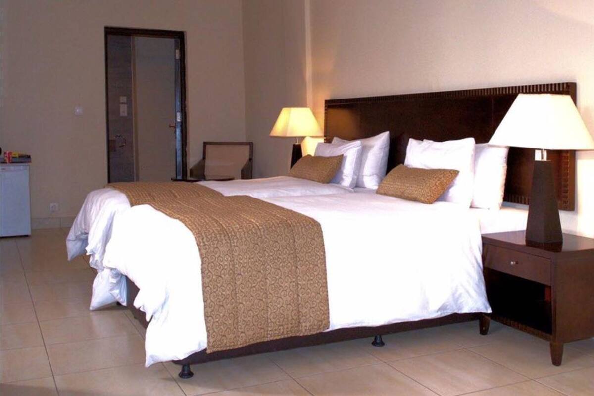 Ein Hotelzimmer mit einem großen Bett, zwei Nachttischlampen, einem Nachttisch und einer Tür.