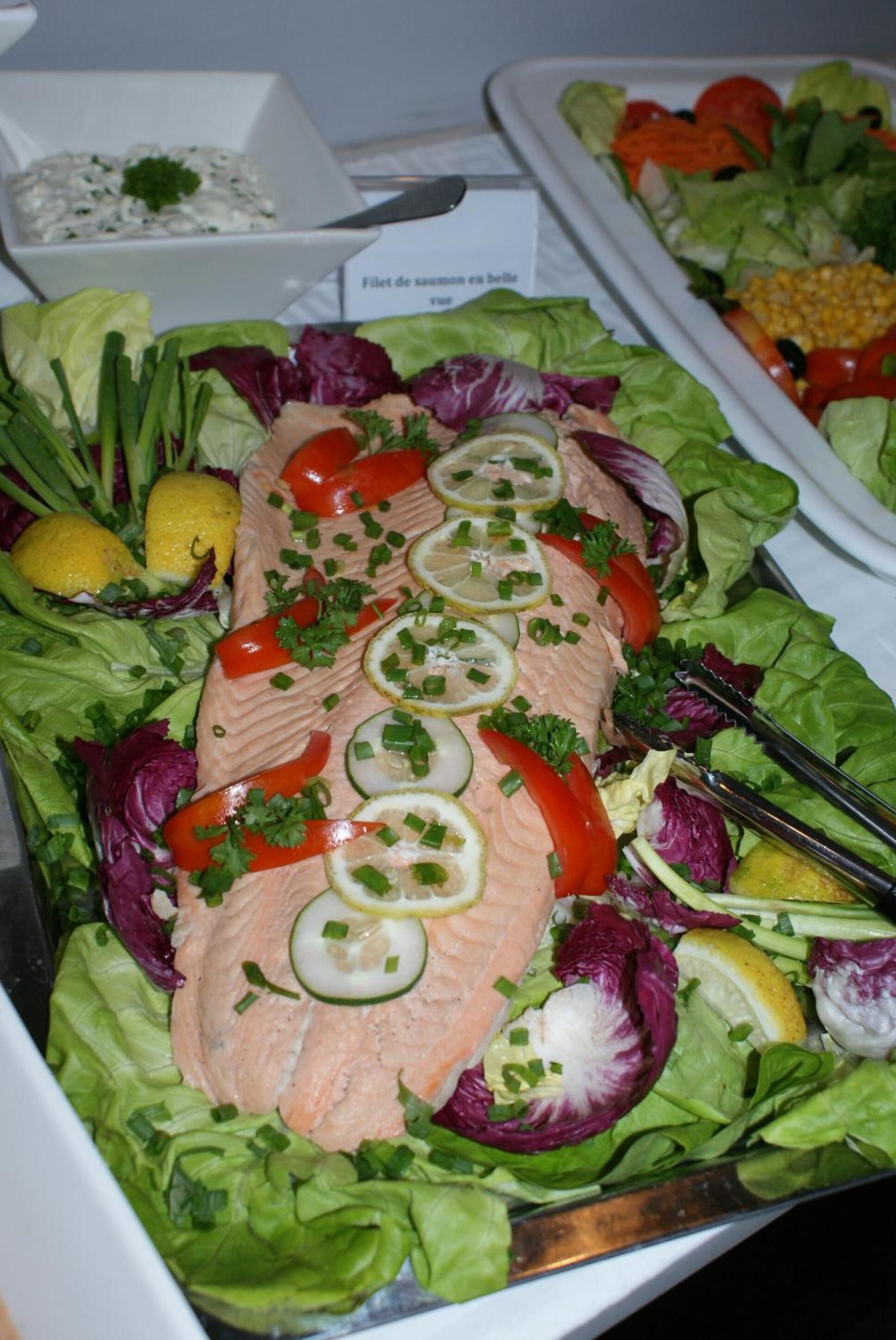 Une assiette de saumon, garnie de tranches de citron et d’herbes aromatiques, entourée d’un mélange de jeunes pousses et de légumes.