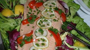 Une assiette de saumon, garnie de tranches de citron et d’herbes aromatiques, entourée d’un mélange de jeunes pousses et de légumes.