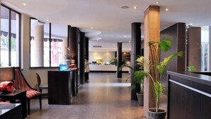 A modern hotel lobby with a reception desk, seating area, and potted plants. - Hotel Royal (Kinshasa)
