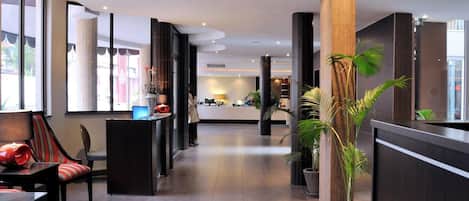 Un hall d’hôtel moderne avec un comptoir d’accueil, un espace salon et des plantes en pot.