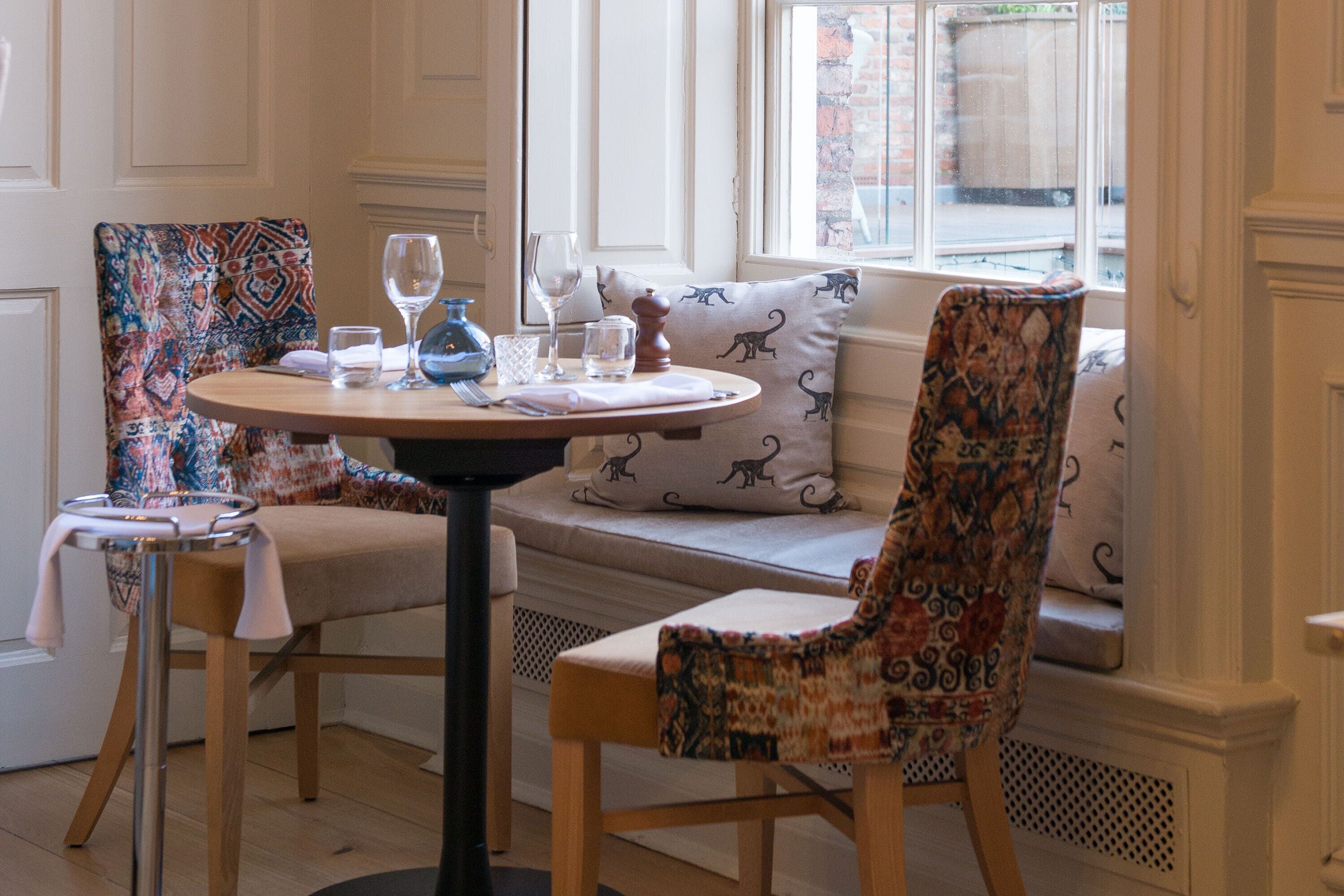 Comedor con una mesa redonda, dos sillas estampadas y un banco con cojines.