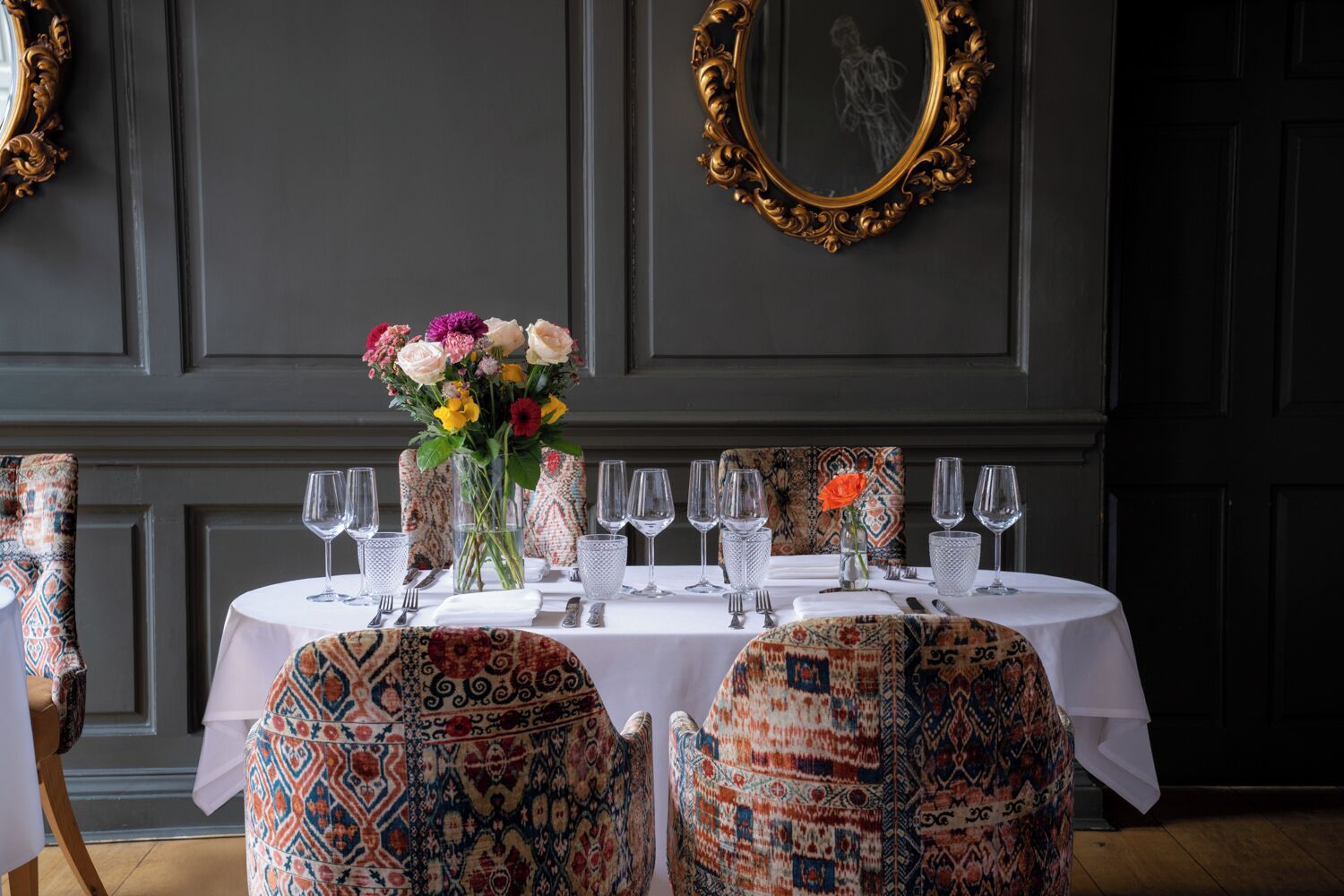 A dining table set with multiple wine glasses, a vase with flowers, and patterned chairs.