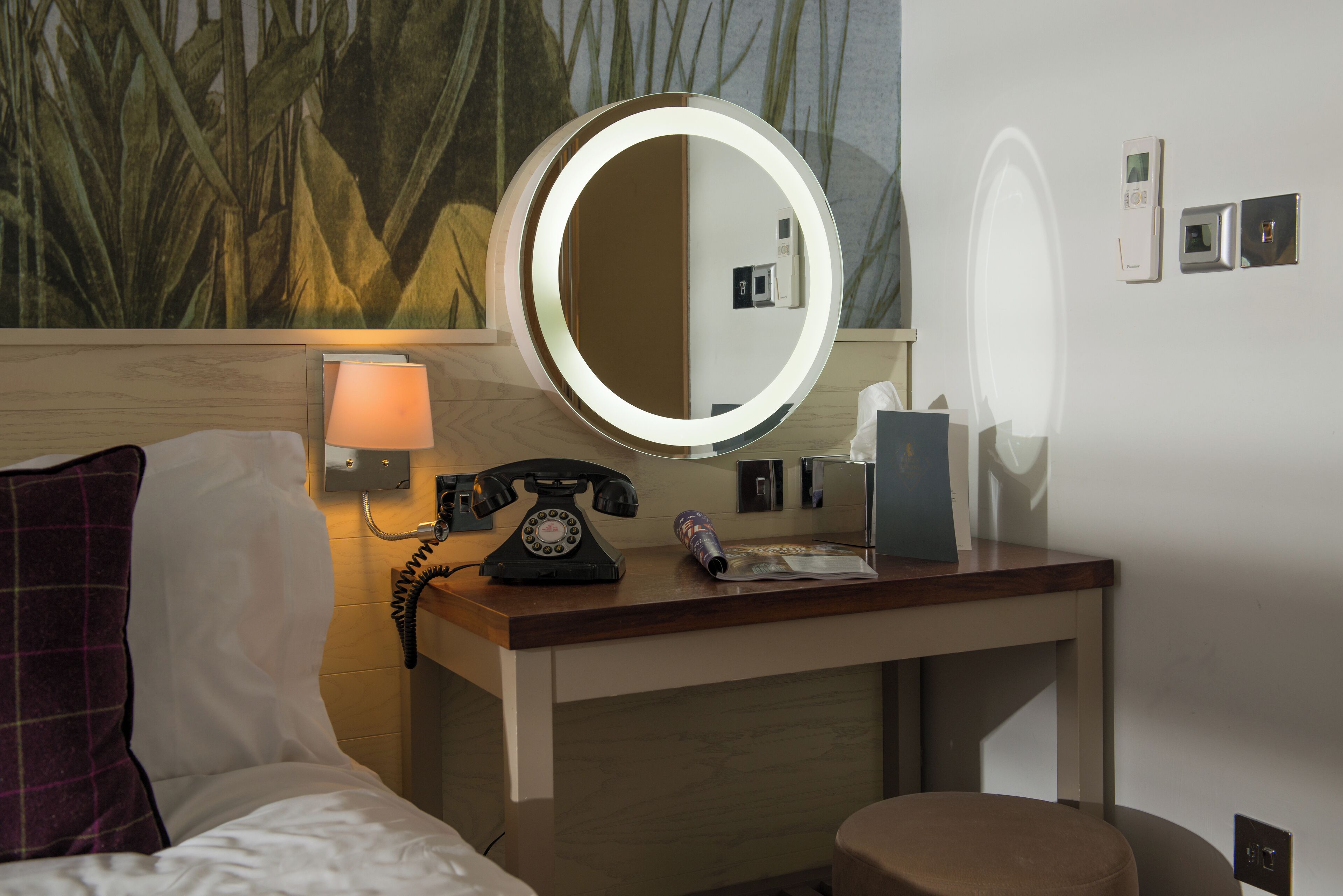 Een hotelkamer met een bed, een bureau met telefoon, een lamp en een spiegel.