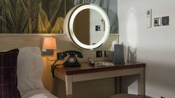 Een hotelkamer met een bed, een bureau met telefoon, een lamp en een spiegel.