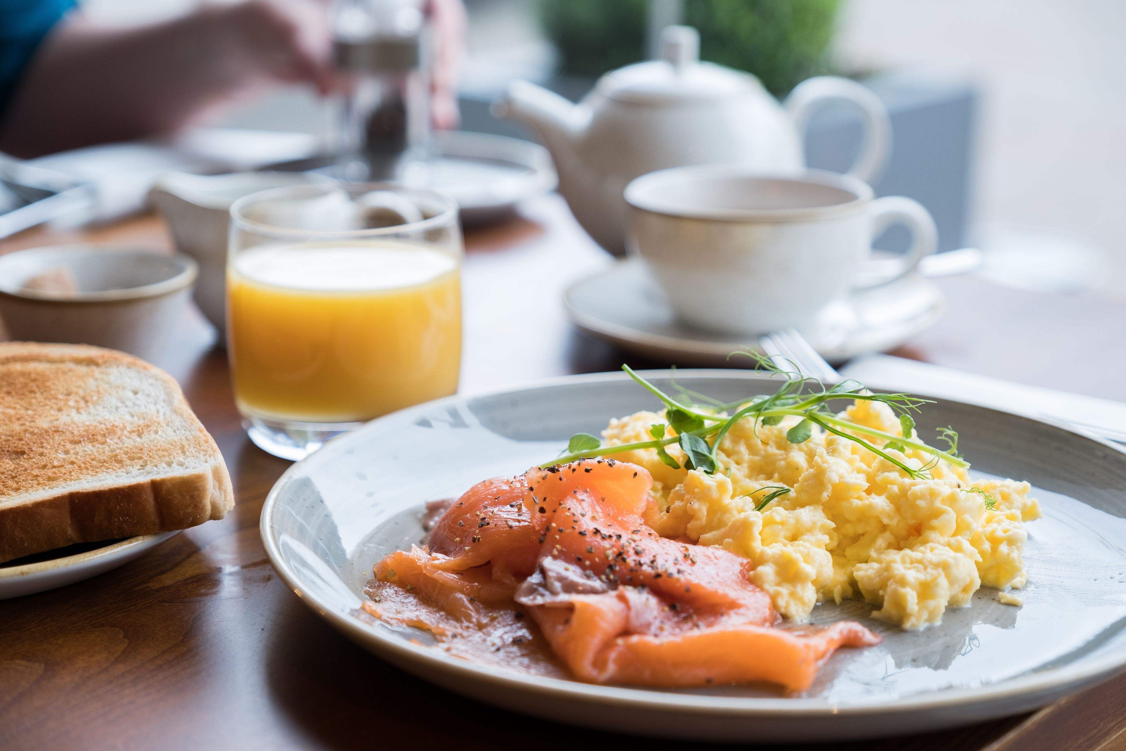 A breakfast plate with scrambled eggs, smoked salmon, and toast on a wooden table.