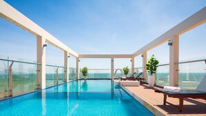 Piscina infinita no terraço, com guarda-corpos de vidro, espreguiçadeiras e plantas em vasos.