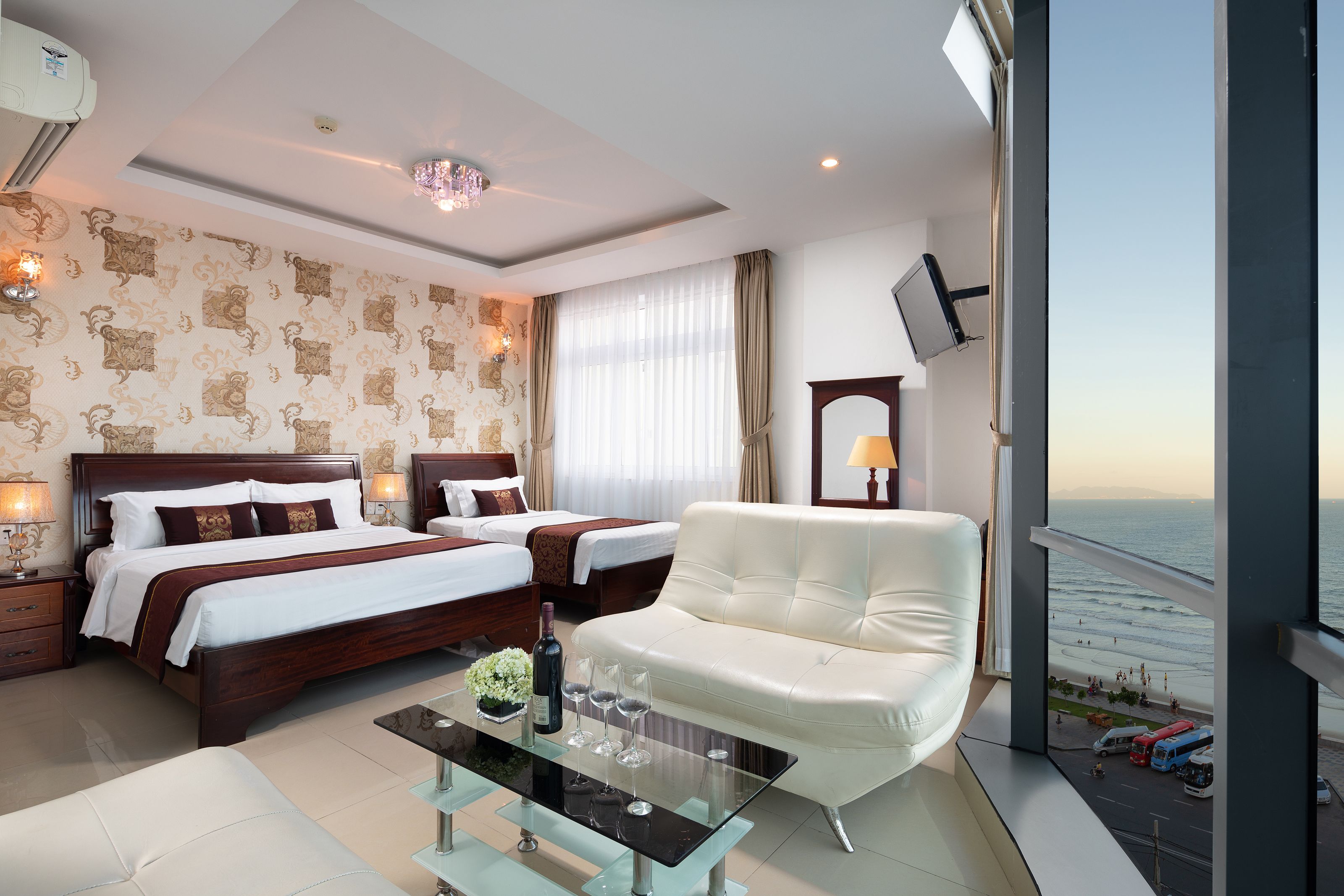 A hotel room with a large bed, a sofa, a glass coffee table, and a view of the beach.
