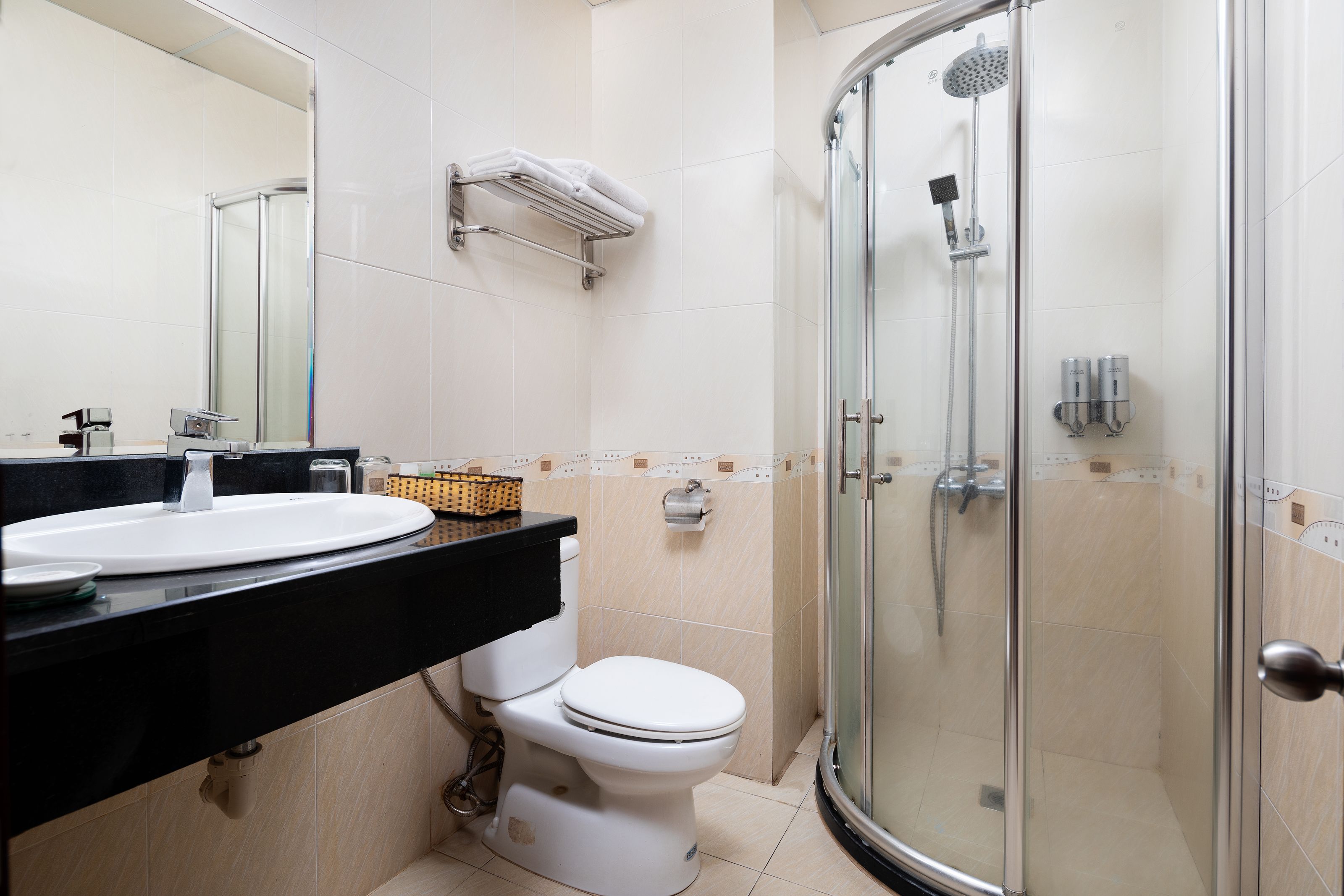 Une salle de bain avec des toilettes blanches, un lavabo noir, une douche en verre et un porte-serviettes.