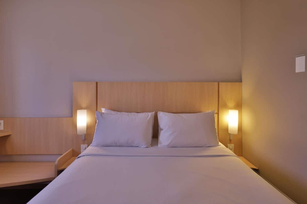 Una habitación de hotel con una cama, dos lámparas de noche y un cabecero de madera.