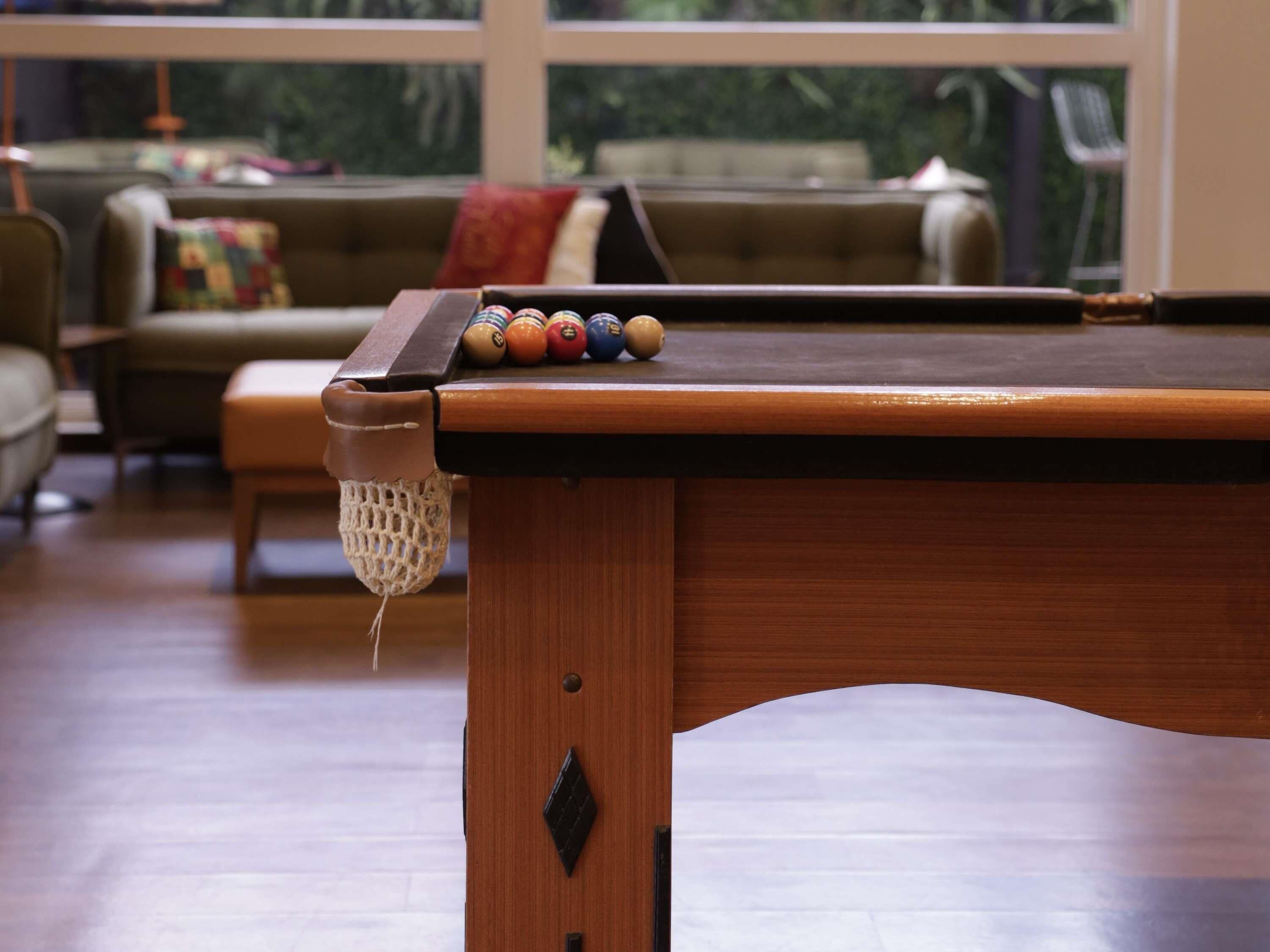 A pool table with balls and a net in a room with a sofa and a window.