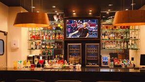 Un espace bar équipé d’un écran de télévision, d’étagères remplies de bouteilles d’alcool et de tabourets de bar.