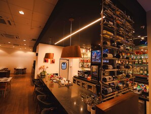 Uma área de bar com um balcão longo, prateleiras cheias de garrafas e uma tela de televisão.