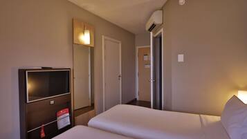 A hotel room with two beds, a TV, a mirror, and an air conditioning unit.