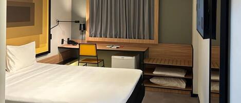Una habitación de hotel moderna con una cama grande, un escritorio, una silla, una mesita, un televisor y un armario.