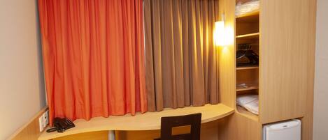 A compact hotel room with a desk, chair, and a small refrigerator.