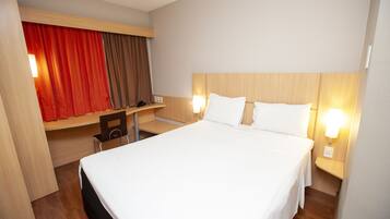 A hotel room with a large bed, a desk, and a chair.