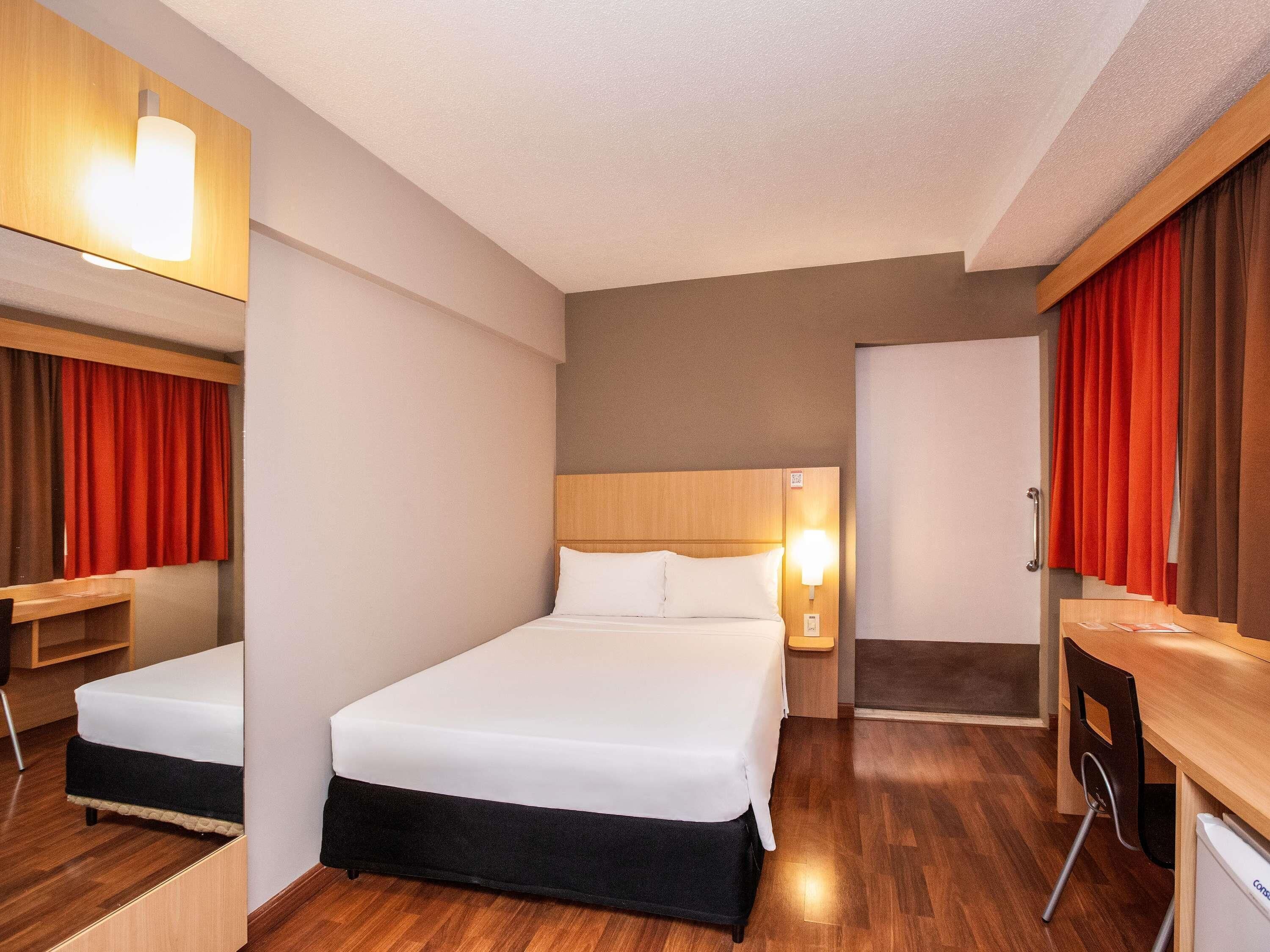 Ein Hotelzimmer mit Bett, Nachttisch, Lampe und Schreibtisch mit Stuhl.