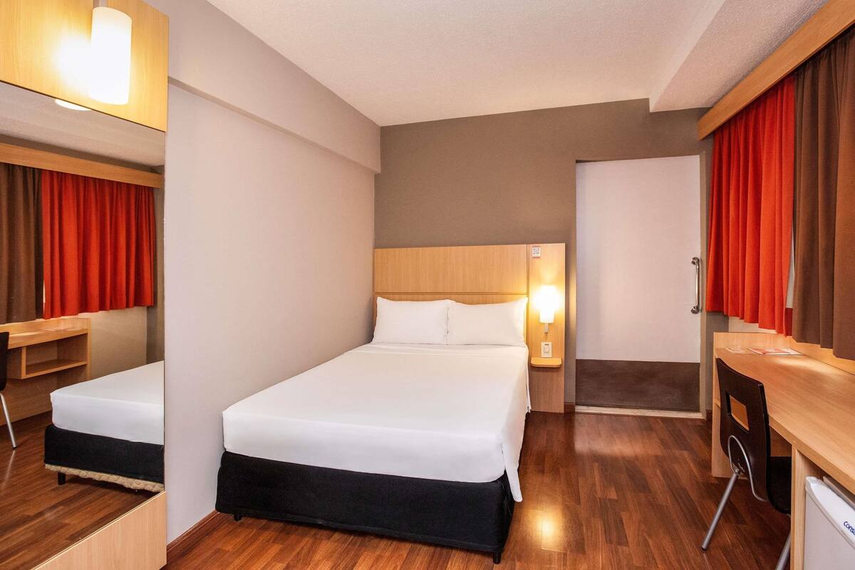 Una habitación de hotel con cama, mesita de noche, lámpara y escritorio con silla.