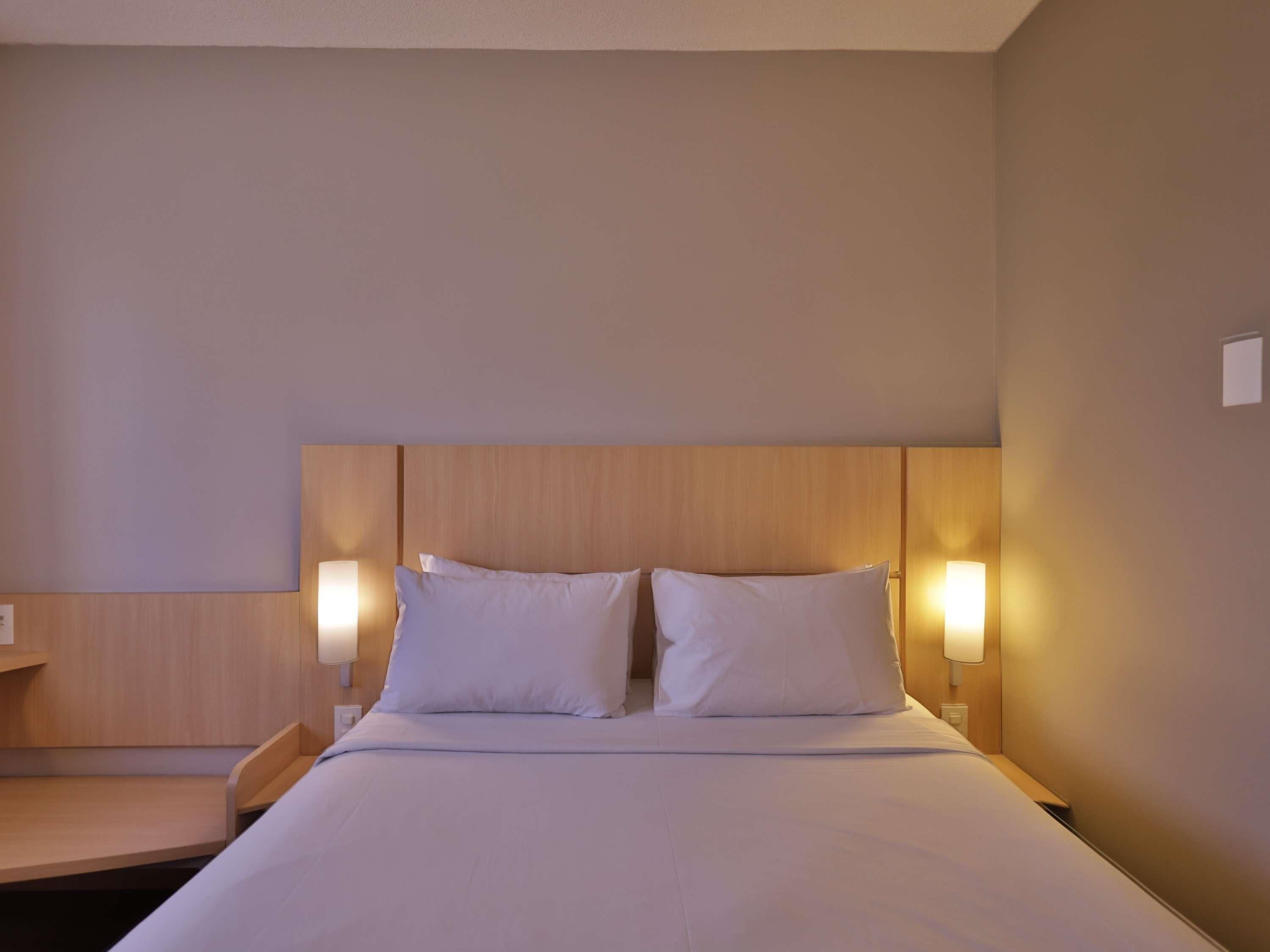 Quarto de hotel com cama, mesas de cabeceira e luminárias fixadas na parede.