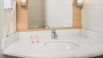 Un baño con lavamanos, espejo, toallero y secador de pelo fijado en la pared.