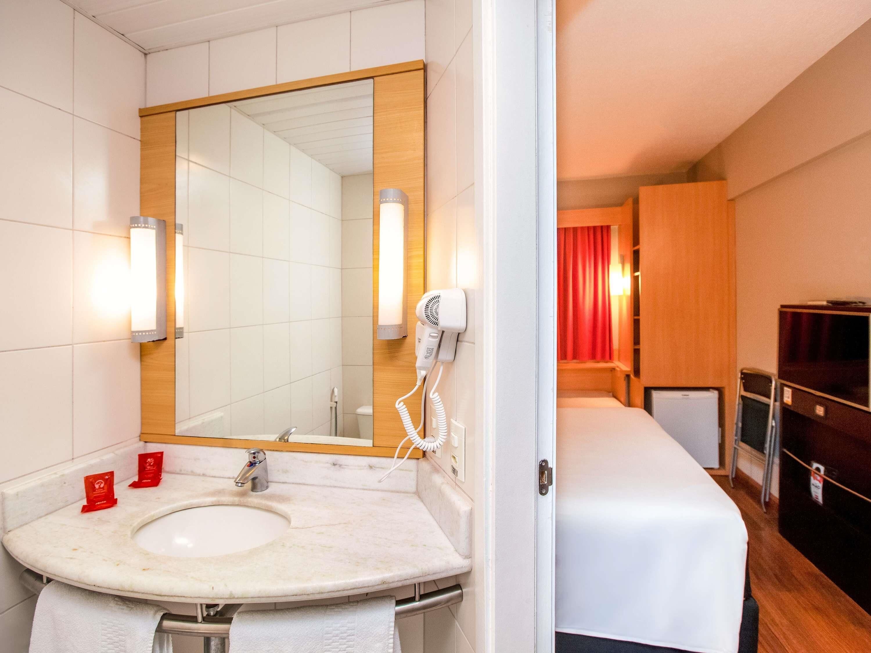 Un baño de hotel con lavamanos, espejo y secador de pelo.