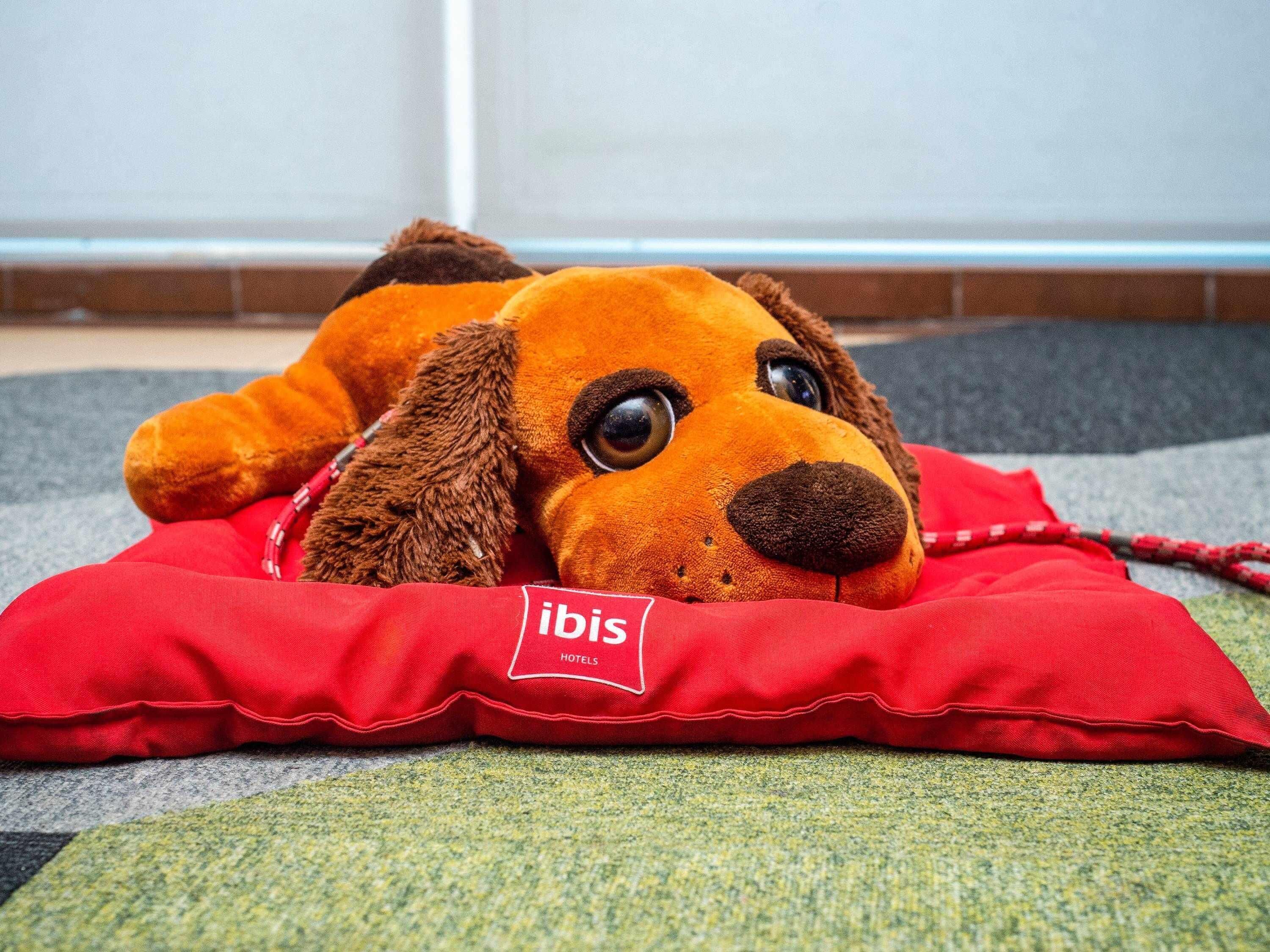 Un jouet en peluche posé sur un coussin rouge, orné du logo « ibis Hotels ».