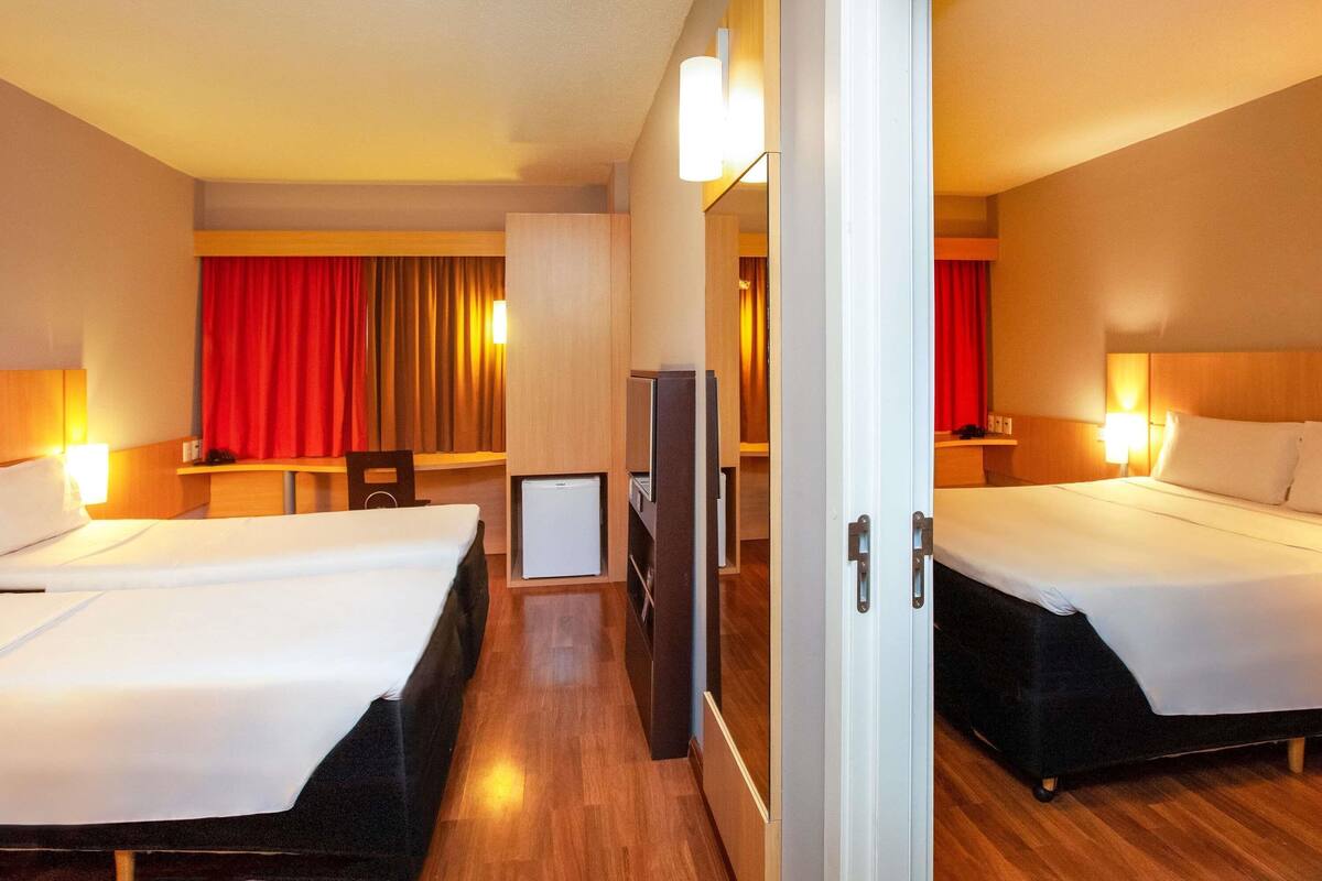 Habitación de hotel con dos camas, un escritorio, un televisor y un espejo.