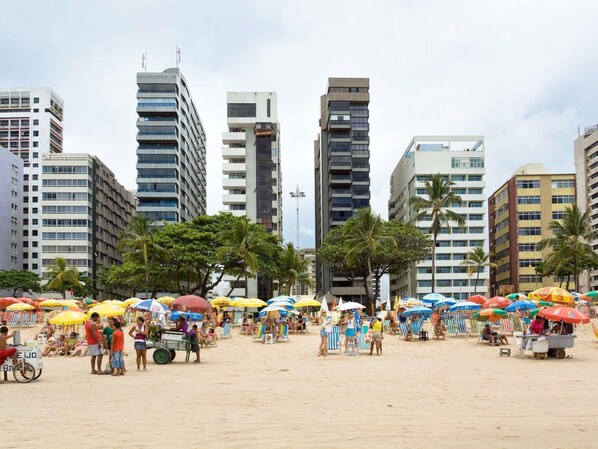 Una playa con gente, sombrillas y edificios altos al fondo.