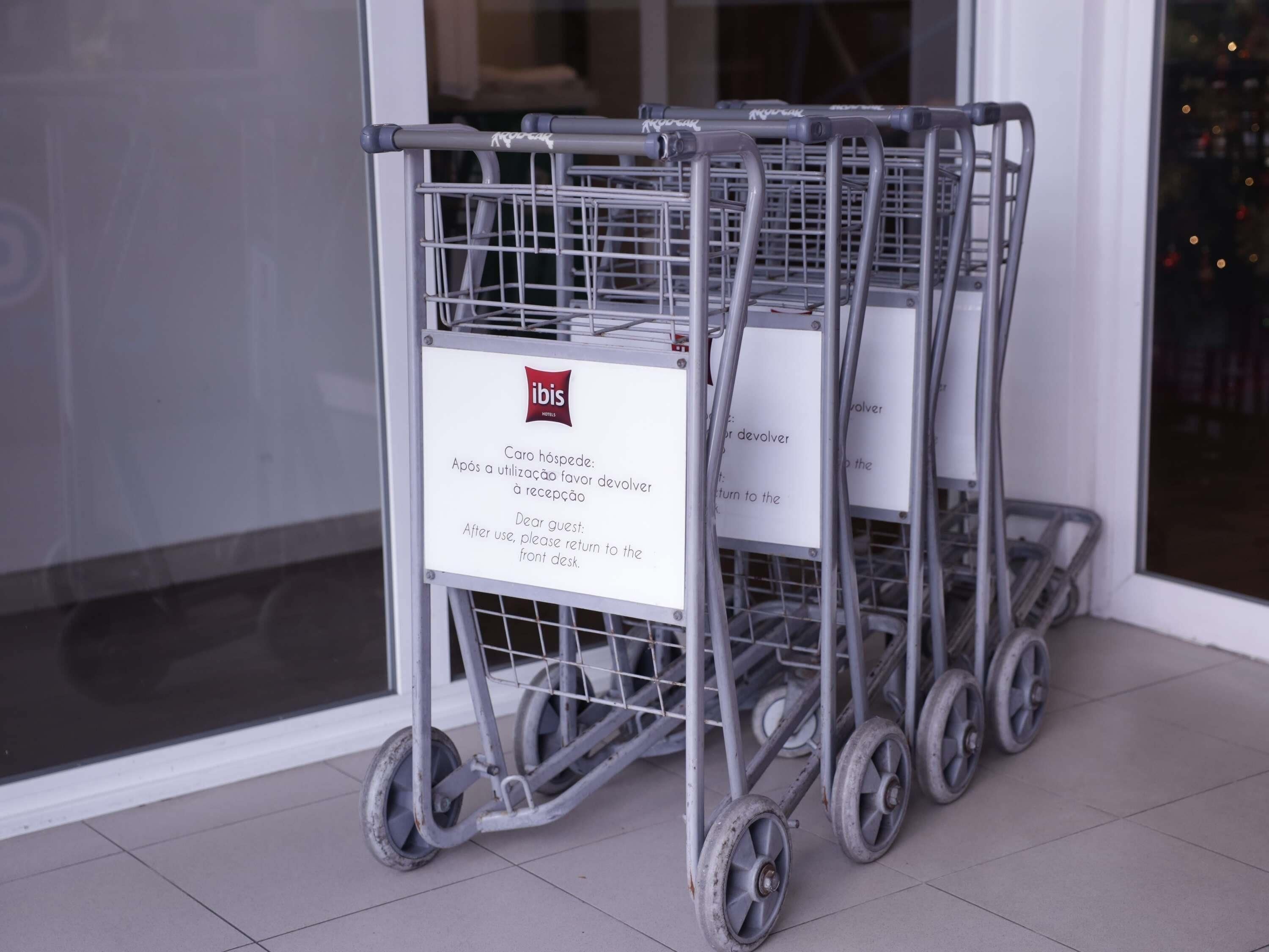 A row of metal shopping carts with a sign attached to one, indicating a return policy for guests.