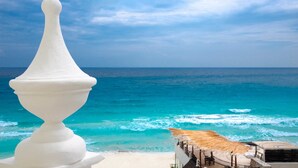 Eine weiße Balustrade mit Blick auf einen Strand, eine strohgedeckte Struktur und eine Meeransicht.