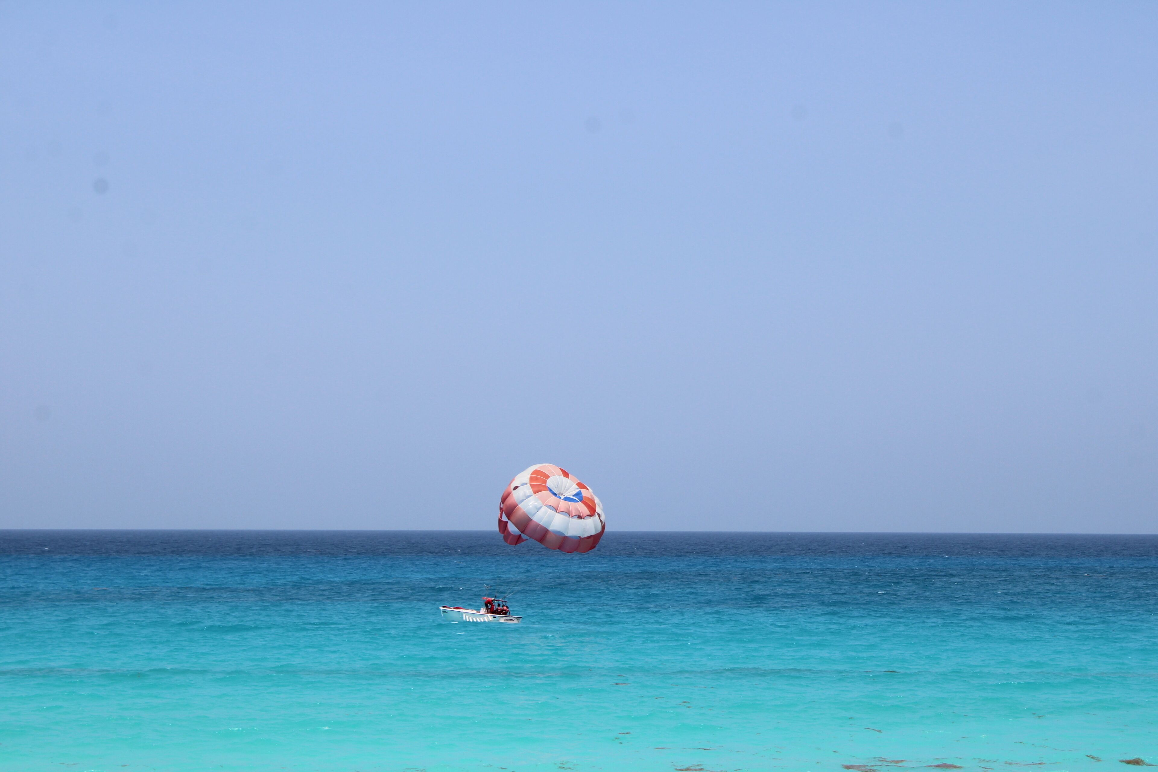 Uma pessoa praticando parasailing sobre águas turquesa, com um pequeno barco por perto.