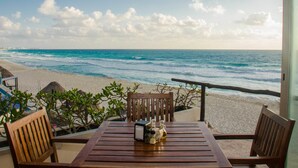 A wooden table with chairs on a balcony overlooking a beach with waves and a clear sky. - Bsea Cancun Plaza Hotel (Cancun)