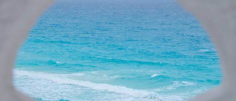 A view through a window of a beach with turquoise water and waves.
