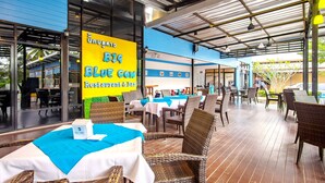 Un espace extérieur aménagé en restaurant, avec des meubles en osier et des tables recouvertes de nappes bleues et blanches.