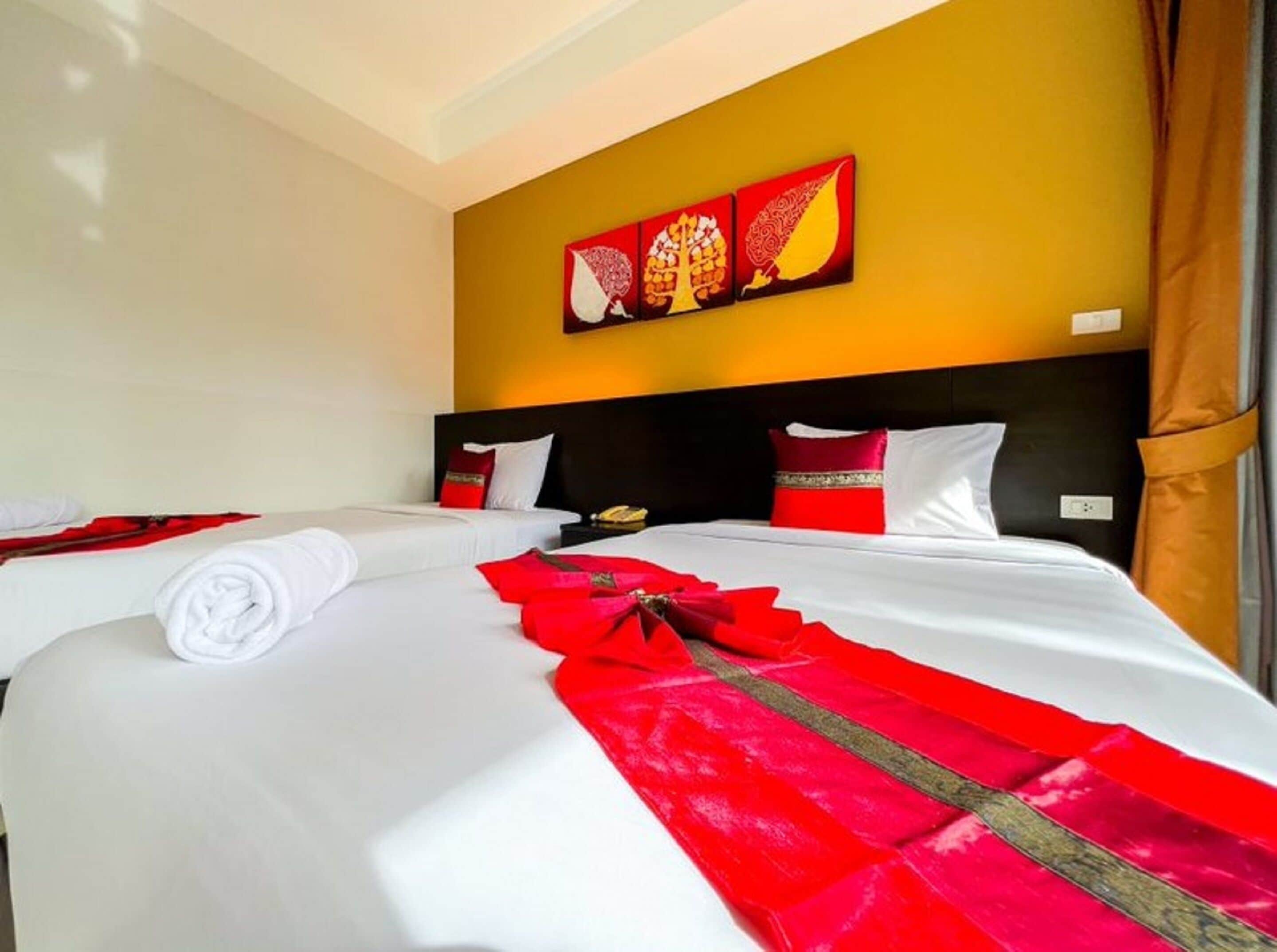 A hotel room with two beds, each with white linens and red decorative elements. There are three paintings on the wall above the beds.