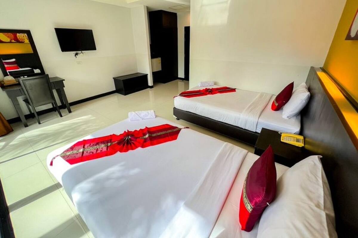 Ein Hotelzimmer mit zwei Betten, einem Schreibtisch, einem Sessel und einem an der Wand befestigten Fernseher.