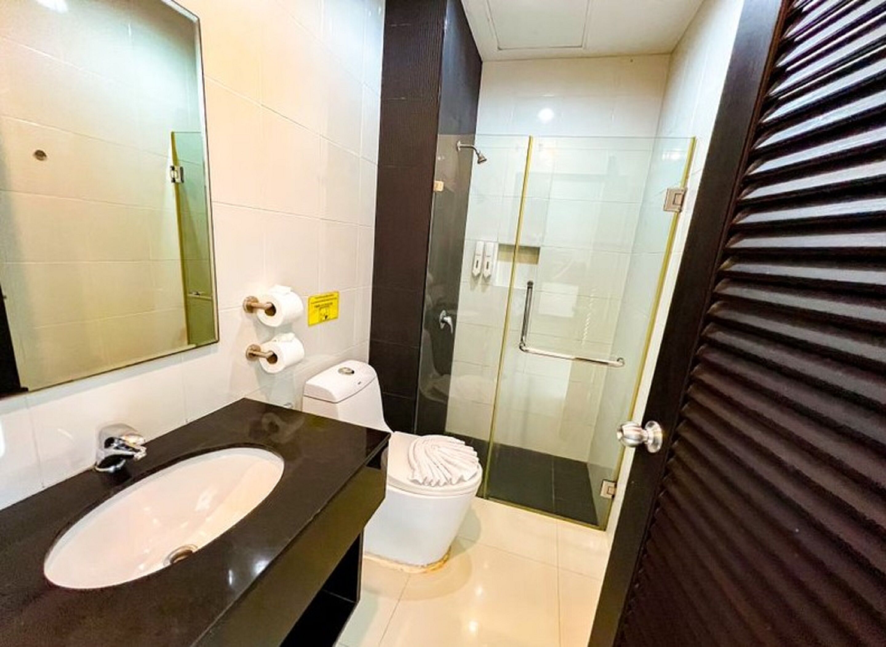 Un baño moderno con un espejo grande, un lavabo, un inodoro y una zona de ducha con mampara de vidrio.
