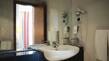Un baño con un lavabo blanco, un espejo y un secador de pelo montado en la pared.