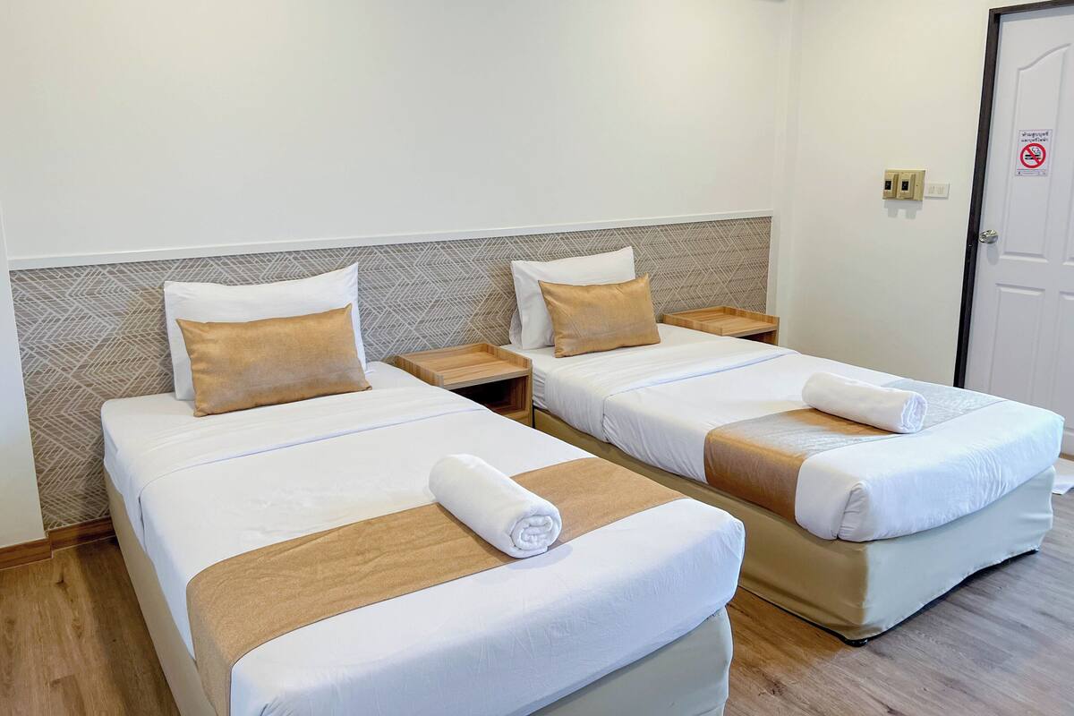 Ett hotellrum med två separata sängar, var och en med ett nattduksbord i trä, vitt sänglinne och en beige accentfärg.