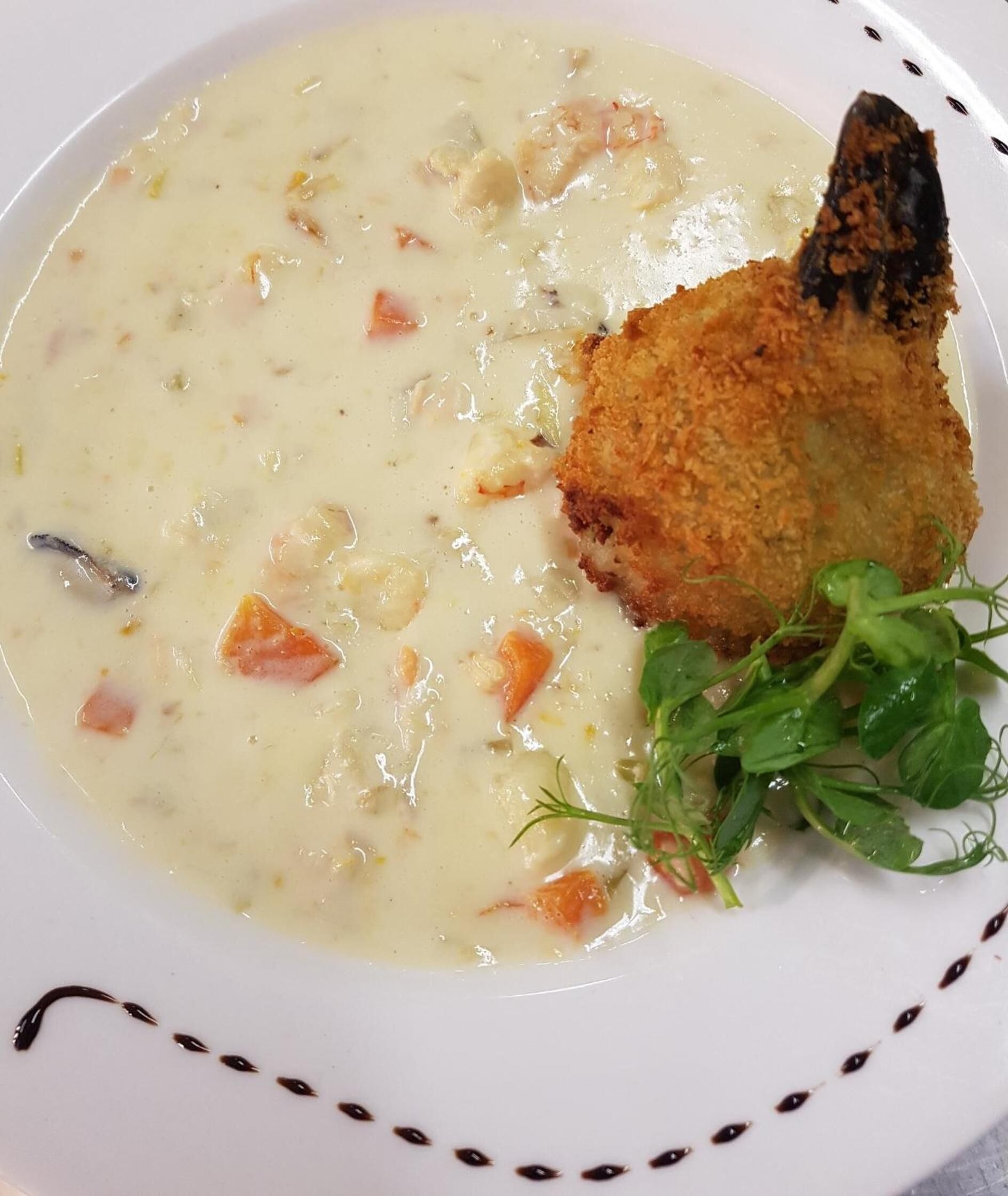 Une assiette de soupe crémeuse contenant des morceaux de légumes et un morceau de poisson pané.