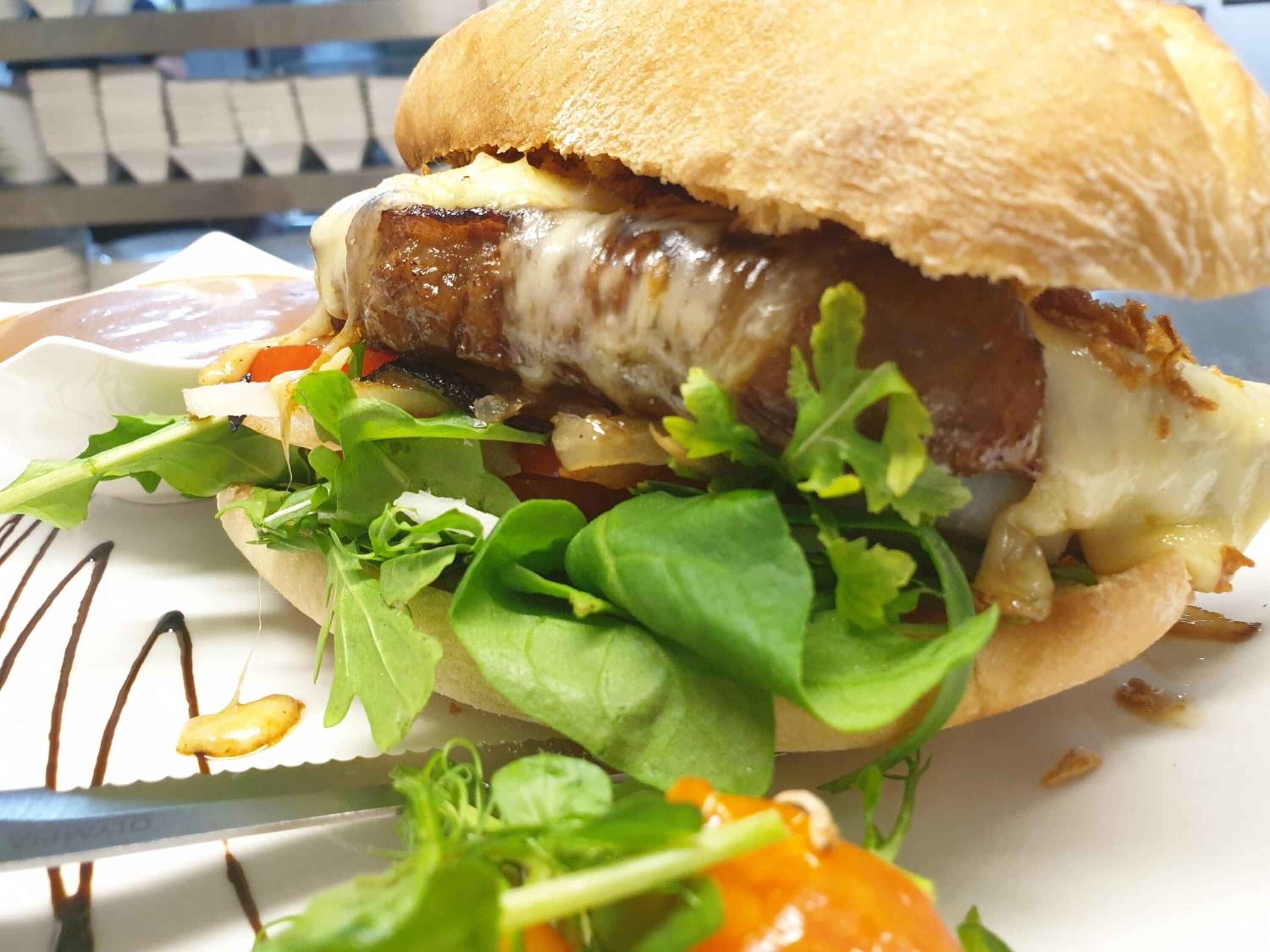 Ein Sandwich mit Brötchen, Fleisch, Käse und Salat auf einem weißen Teller.