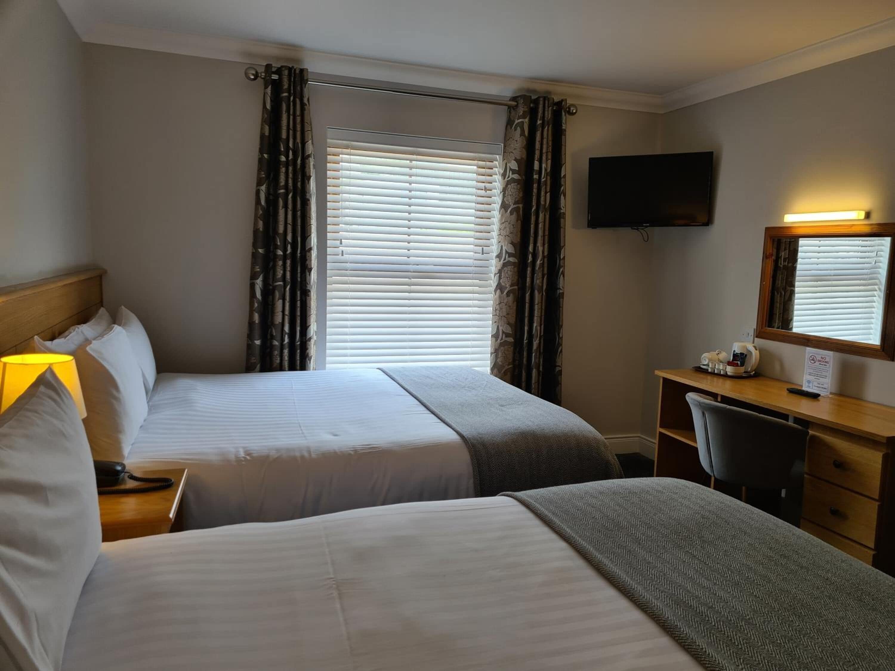 A hotel room with two beds, a desk, a chair, a TV, and a window with blinds.