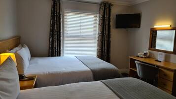 A hotel room with two beds, a desk, a chair, a TV, and a window with blinds.