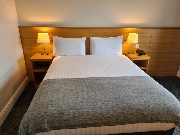 A hotel room with a large bed, two bedside tables with lamps, a telephone, and a wooden headboard. - Caisleain Oir Hotel (Annagry)