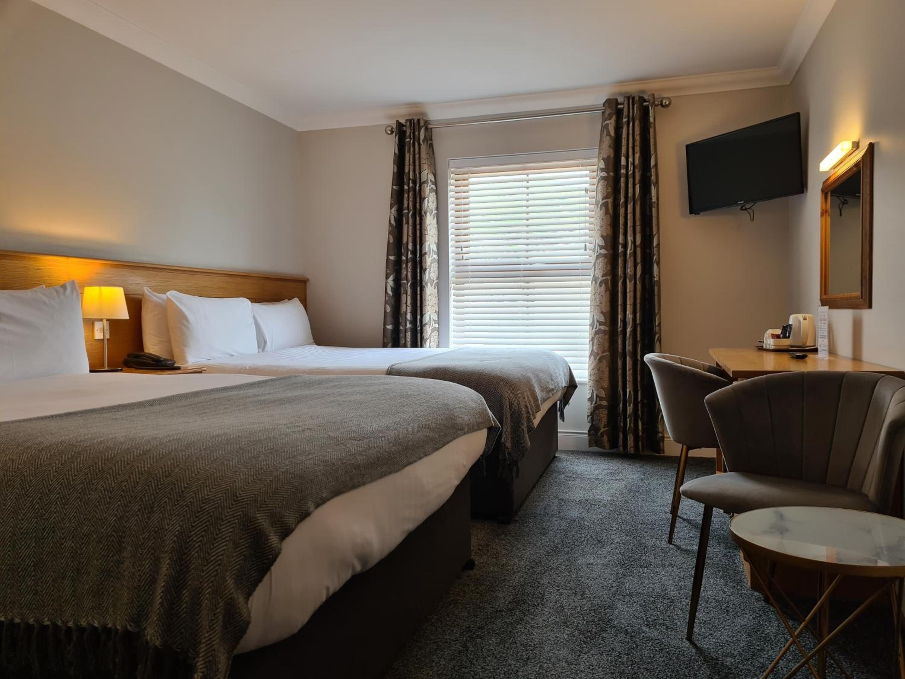 A hotel room with two beds, a desk with a chair, a television, and a window with blinds.