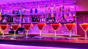 Un bar avec plusieurs verres à martini remplis de cocktails rouges, une variété de bouteilles d’alcool exposées sur des étagères et un comptoir.